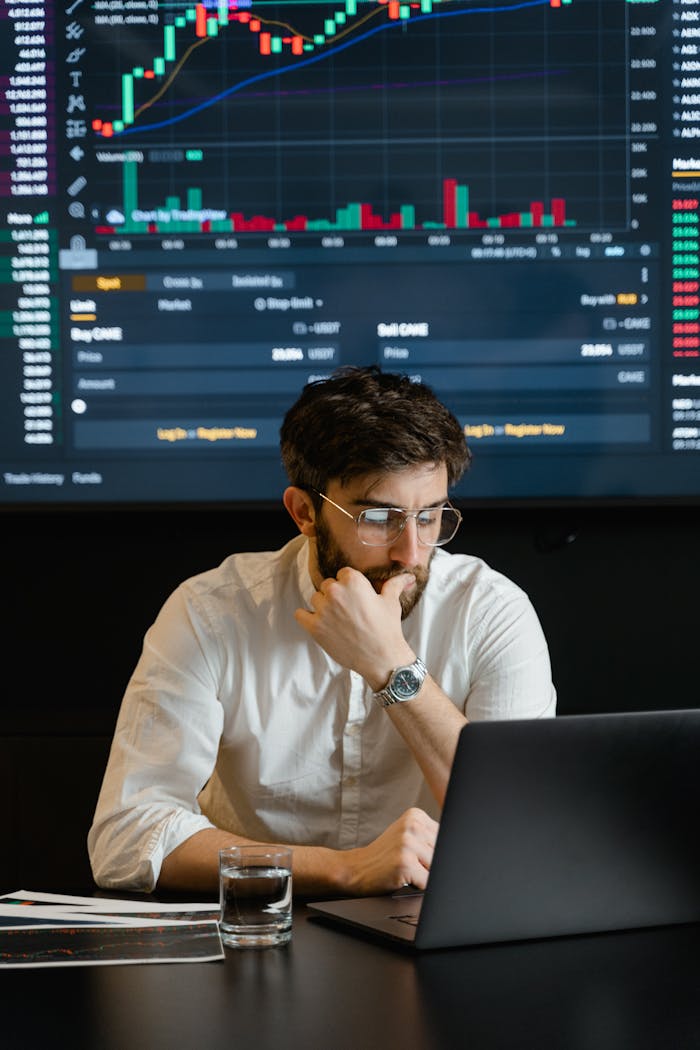 Pensive businessman with a beard analyzing stock market trends on a laptop in an office setting.